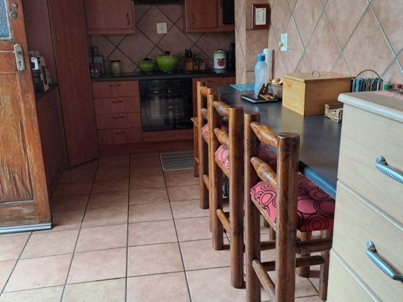A functional kitchen featuring wooden cabinetry, a built-in oven with hob, tiled flooring, and a breakfast bar area.