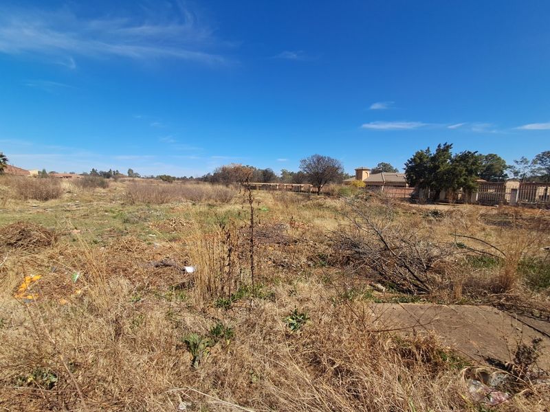 A view of a vacant residential plot featuring dry, overgrown vegetation and perimeter fencing, offering a blank canvas for future development.