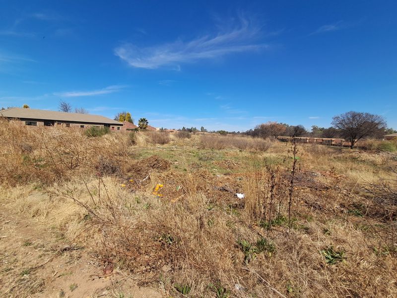 A view of a vacant residential plot featuring dry, overgrown vegetation and open land, suitable for future development.