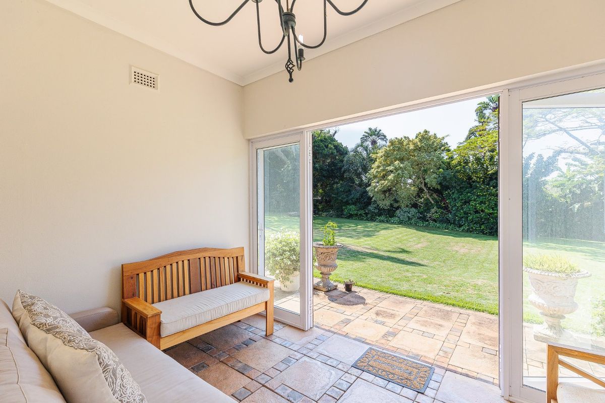 A bright sunroom featuring tiled flooring and large sliding glass doors that open directly onto a spacious rear garden and patio area.