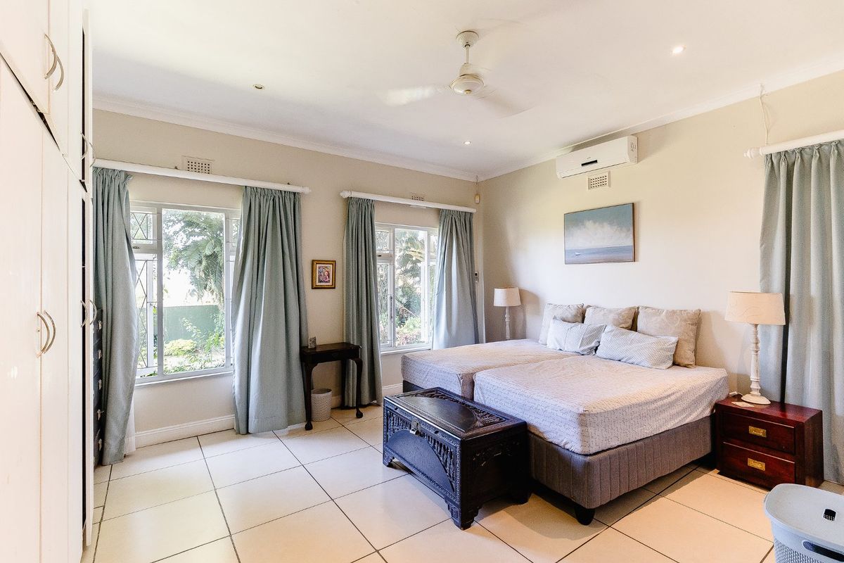Spacious bedroom featuring tiled flooring, built-in cupboards, ceiling fan, and wall-mounted air conditioning unit with large windows providing natural light.