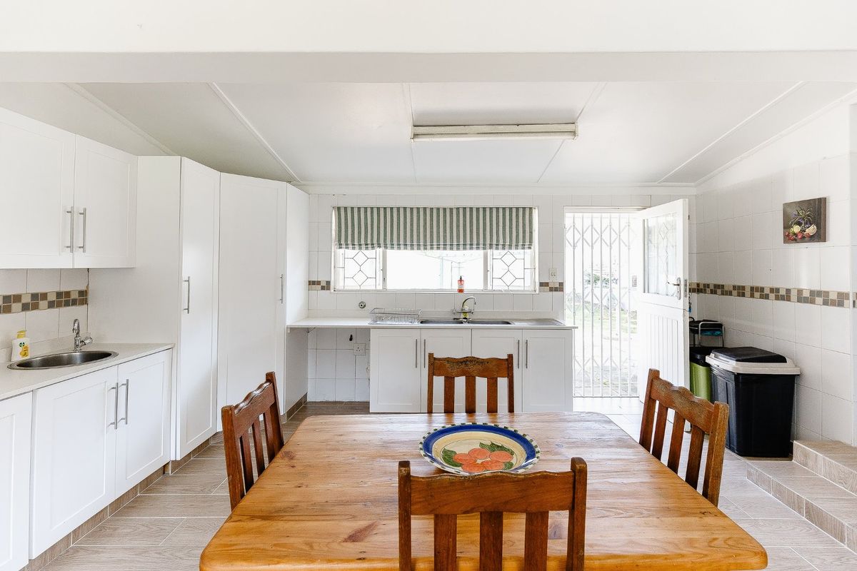 A functional kitchen featuring white cabinetry, tiled splashbacks, dual sink areas, and direct access to the exterior through a security gate.