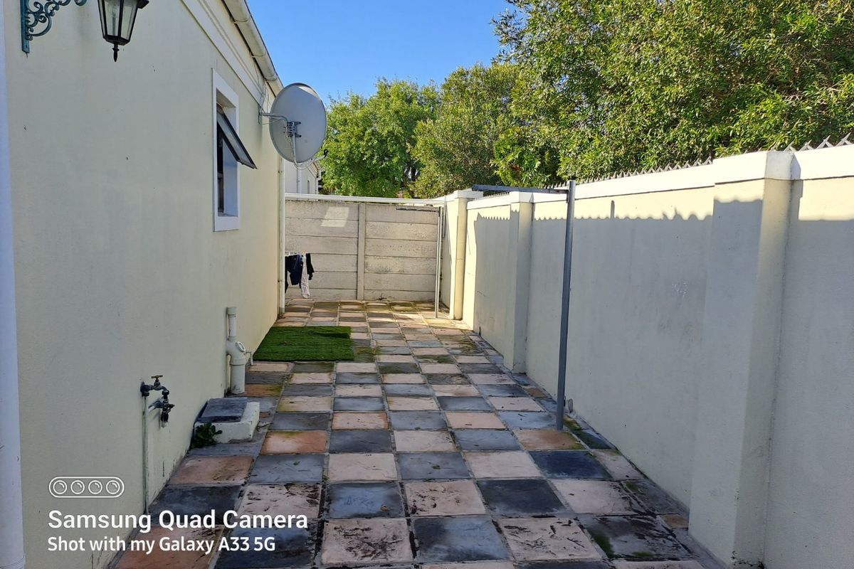 A narrow rear exterior courtyard featuring a tiled patio, boundary walls, and external utility fixtures.