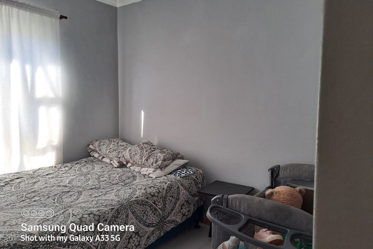 A standard bedroom featuring neutral grey walls and natural light from a window with a curtain rod.
