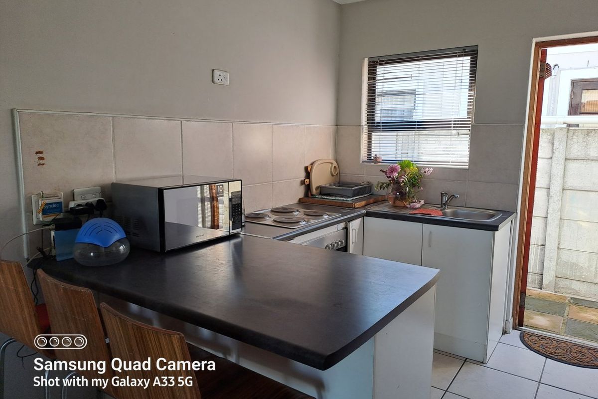 Compact kitchen featuring built-in cabinetry, a laminate countertop, electric hob, and tiled backsplash with direct access to an outdoor area.