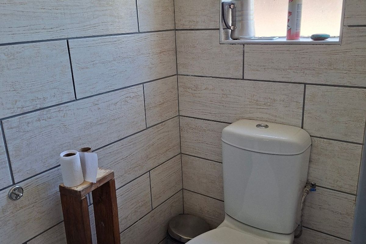 A compact bathroom featuring light-toned wood-look wall tiles, a decorative mosaic border, a white toilet, and a frosted glass window for privacy.