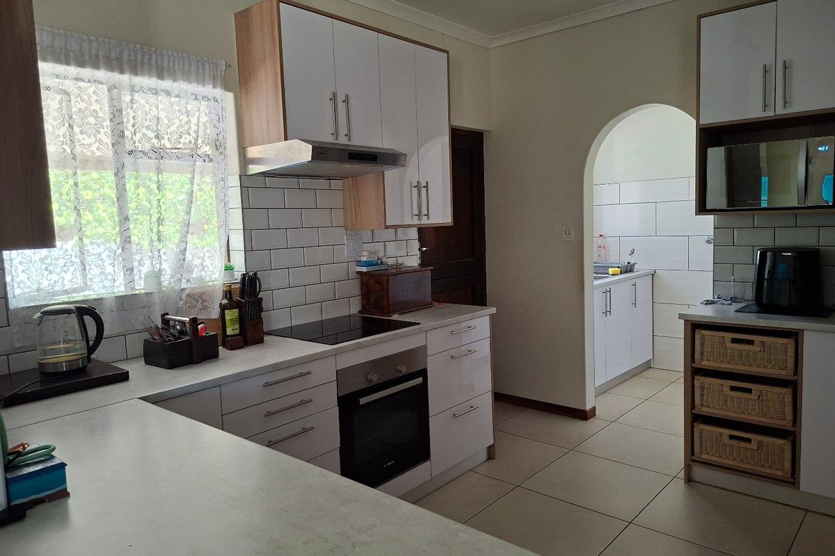 Modern kitchen featuring white cabinetry, subway tile backsplash, built-in oven and hob, with an adjoining scullery area through an arched doorway.