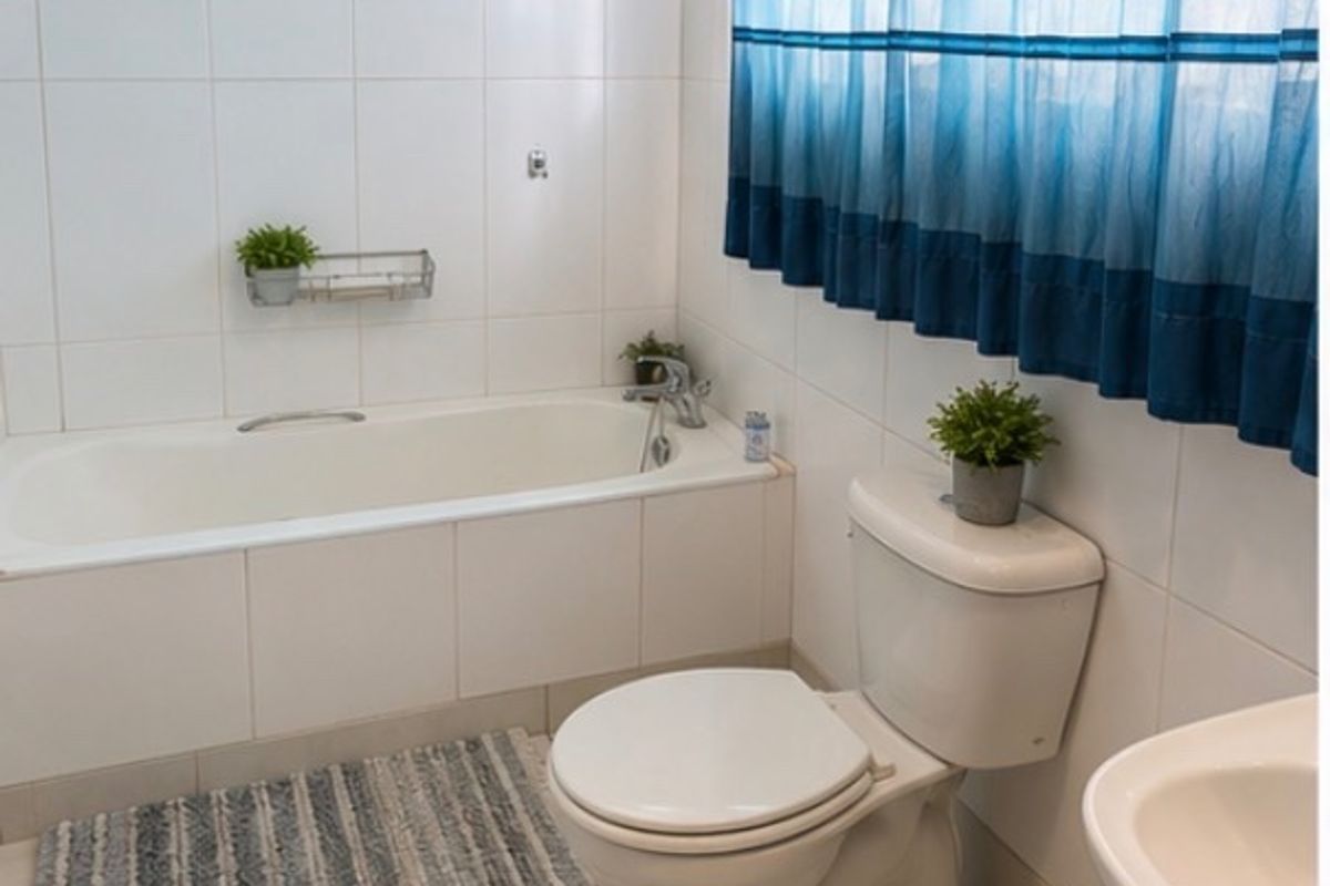 A functional bathroom featuring a standard bathtub, toilet, and washbasin with neutral wall and floor tiling.
