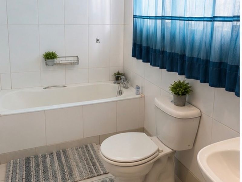 A functional bathroom featuring a standard bathtub, toilet, and washbasin with neutral wall and floor tiling.