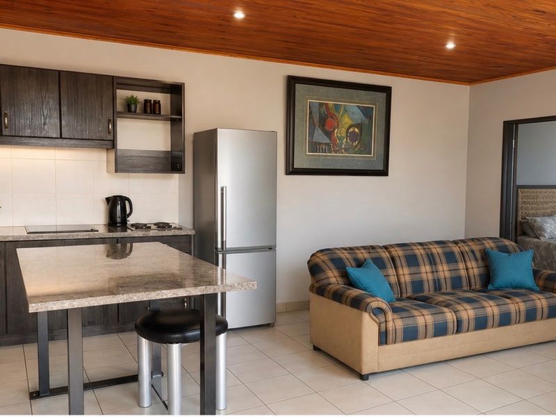 An open-plan living area featuring a modern kitchen with dark cabinetry, granite countertops, and a wood-paneled ceiling, seamlessly connected to a comfortable lounge space.