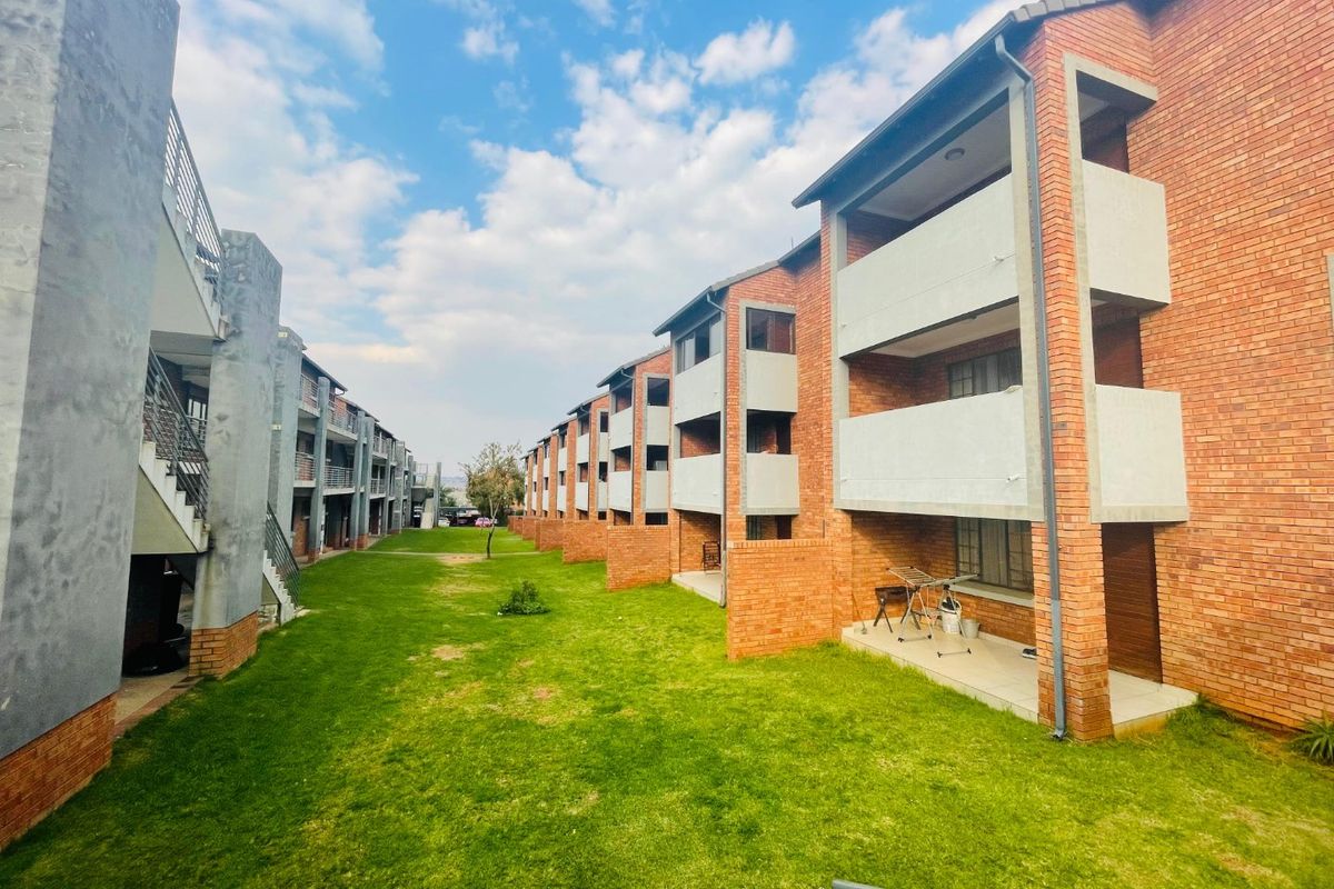 Exterior view of a multi-story apartment complex featuring brick facades, private balconies, and a shared central lawn area.