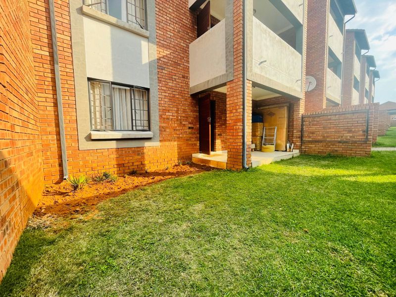 Rear view of a face brick apartment building featuring a covered patio area and a private lawn space.