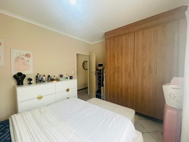A well-maintained bedroom featuring neutral walls, tiled flooring, and a large built-in wooden wardrobe providing ample storage space.