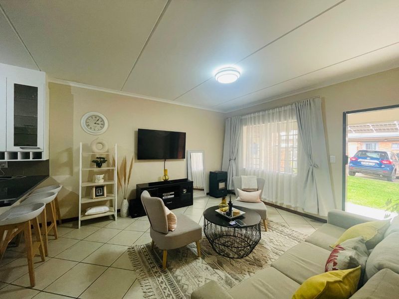 An open-plan living area featuring tiled flooring, a compact kitchen with breakfast bar, and direct access to the exterior.