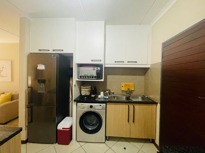 Compact kitchen area featuring white upper cabinetry, wood-finish lower cabinets, a double sink, and tiled backsplash with integrated appliance space.