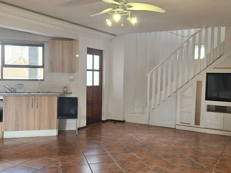 Open-plan living area featuring a kitchen with built-in cabinetry, a wood-burning stove, and a staircase leading to the upper level.
