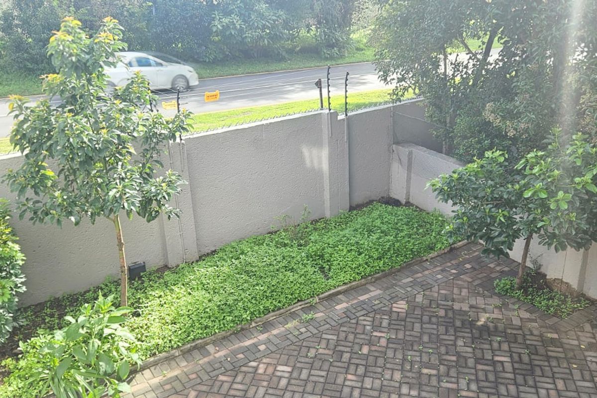 A private rear courtyard featuring a paved patio area, established garden beds, and a secure boundary wall with integrated electric fencing.