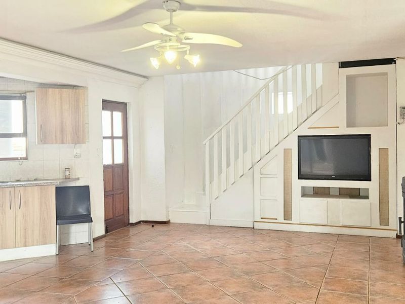 Open-plan living area featuring a kitchen, staircase, and wood-burning stove, with tiled flooring throughout.