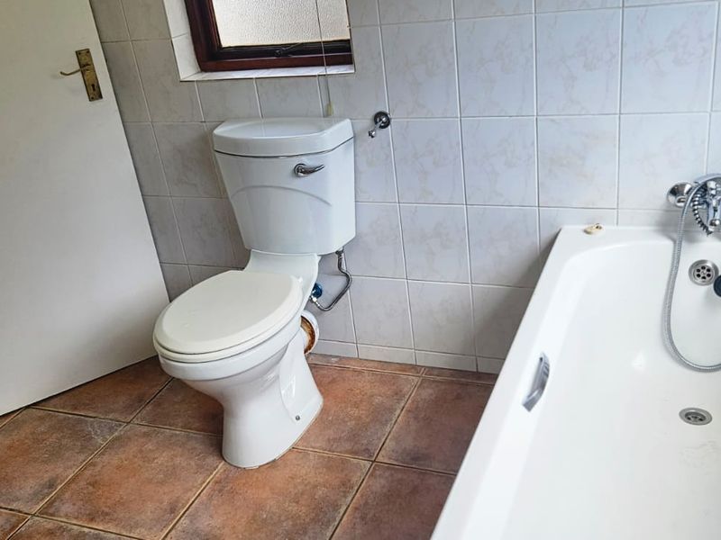 A functional bathroom featuring a standard bathtub with handheld shower mixer, ceramic wall and floor tiling, and a white toilet.