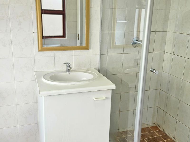 A functional bathroom featuring a vanity with a drop-in basin, a glass-enclosed shower, and neutral wall tiling.