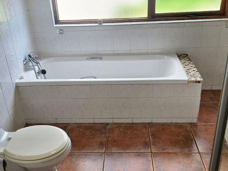 A functional bathroom featuring a built-in bathtub, toilet, and vanity basin with tiled flooring and wall finishes.