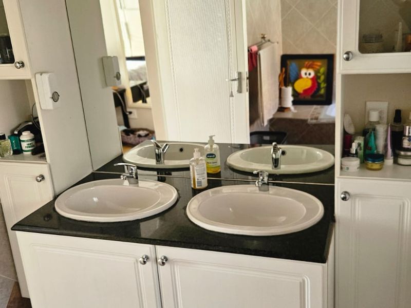 A functional bathroom featuring a double vanity with granite countertops, dual drop-in sinks, and integrated storage cabinetry with a large wall mirror.