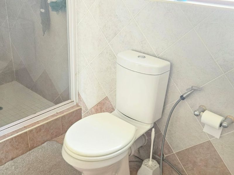 A functional bathroom featuring a standard toilet, a shower enclosure with glass door, and neutral wall and floor tiling.
