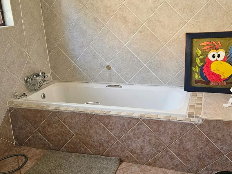A functional bathroom featuring a built-in bathtub with tiled surround, ceramic wall and floor tiling, and standard sanitary fixtures.