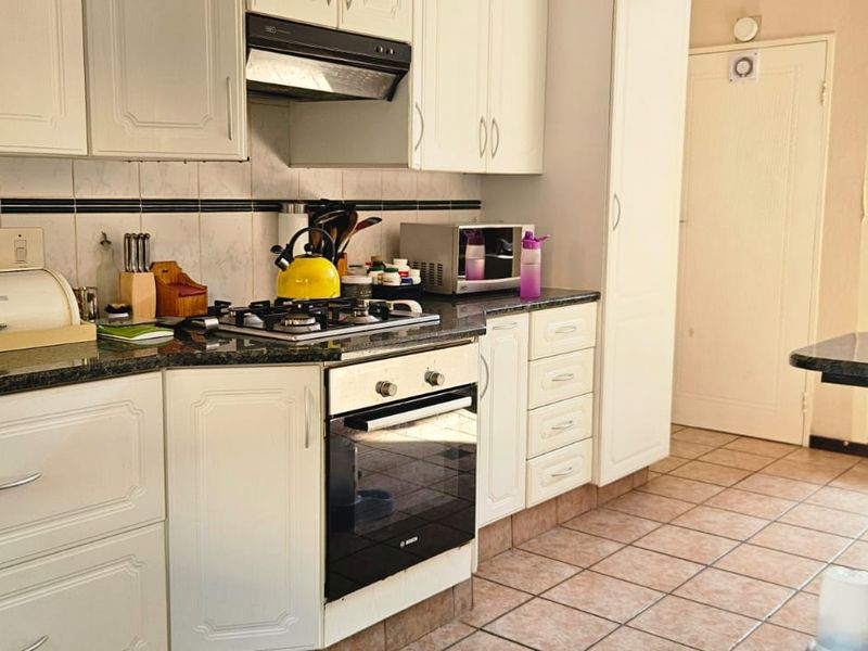 A functional kitchen featuring white cabinetry, granite countertops, a gas hob, built-in oven, and tiled flooring, offering a practical layout for daily use.