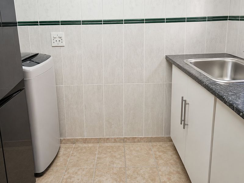 A functional laundry area featuring built-in cabinetry, a stainless steel sink, laminate countertops, and tiled finishes.