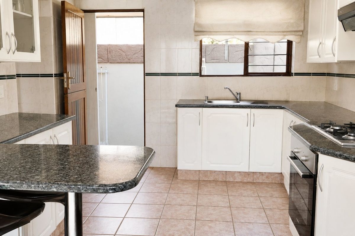 A functional kitchen featuring granite countertops, built-in cabinetry, a gas hob, and an integrated oven, with direct access to an outdoor area.