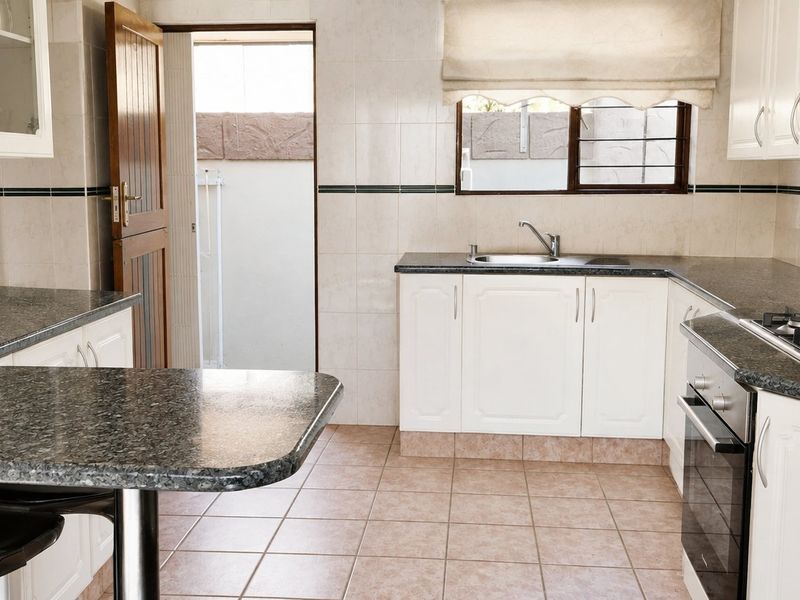 A functional kitchen featuring granite countertops, built-in cabinetry, a gas hob, and an integrated oven, with direct access to an outdoor area.