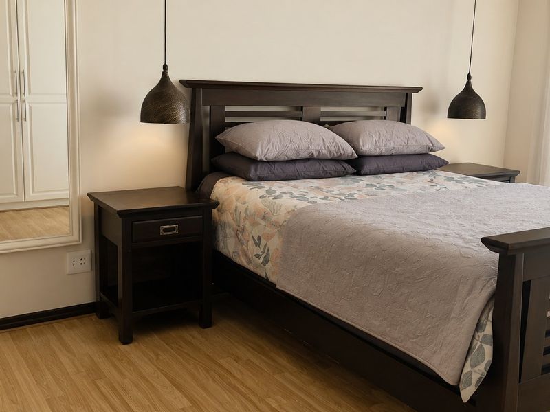 A well-maintained bedroom featuring laminate flooring, built-in wardrobe storage, and modern pendant lighting.