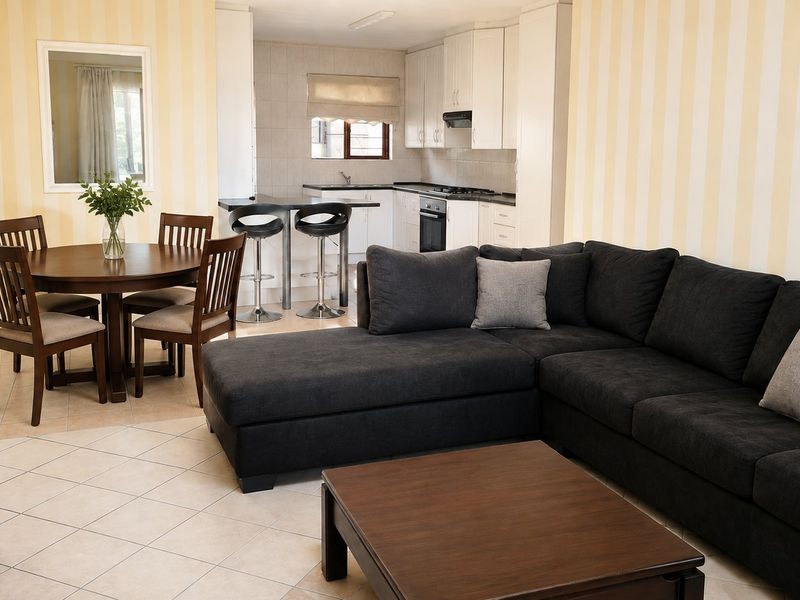 Open-plan living and dining area featuring a functional kitchen with built-in cabinetry, oven, hob, and a breakfast bar, finished with neutral tiled flooring.