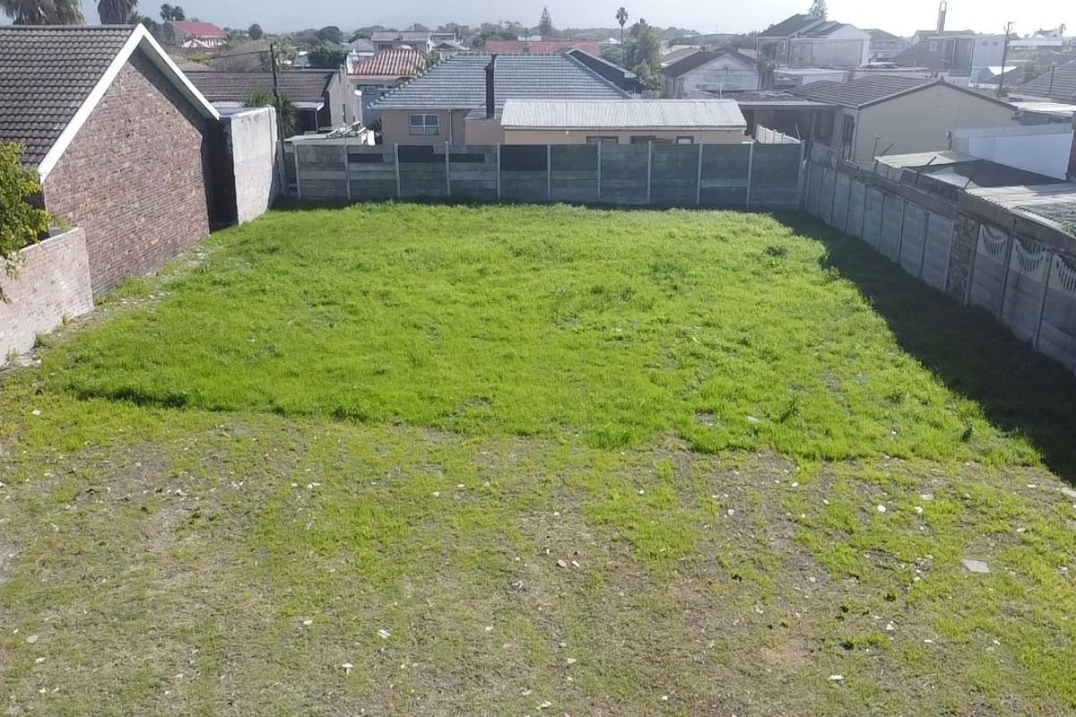 A vacant residential plot featuring a grassed area enclosed by precast concrete and brick boundary walls in a suburban setting.