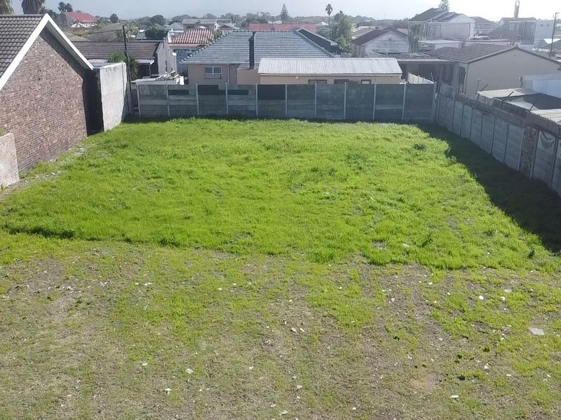 A vacant residential plot featuring a grassed area enclosed by precast concrete and brick boundary walls in a suburban setting.