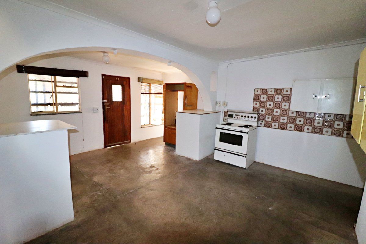 An empty kitchen area featuring an arched entryway, a freestanding stove, tiled splashback, and concrete flooring, offering significant potential for renovation and modernization.