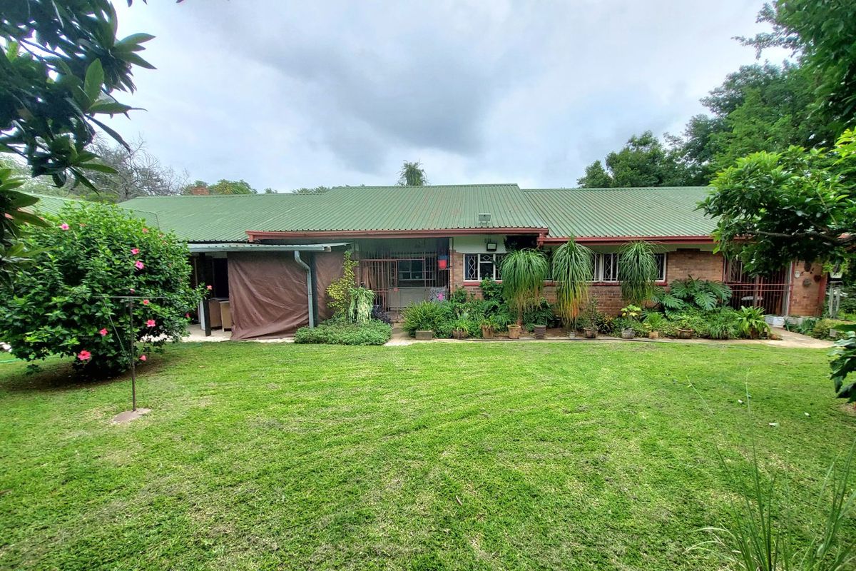 Rear view of a single-story brick farmhouse featuring a green corrugated metal roof, security bars on windows, and a spacious established lawn.