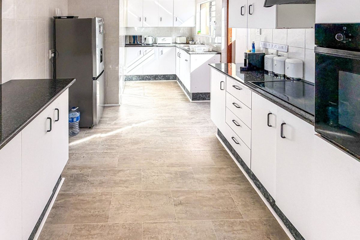 A functional kitchen featuring white cabinetry, dark granite countertops, built-in oven, electric hob, and tiled flooring with ample workspace.