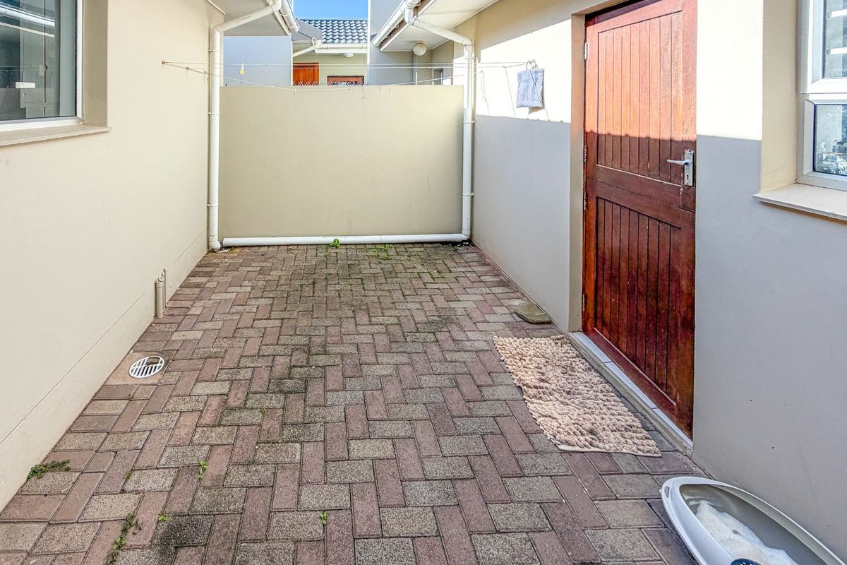 A paved rear courtyard area featuring a timber door entrance, drainage, and guttering, providing a functional outdoor utility space.