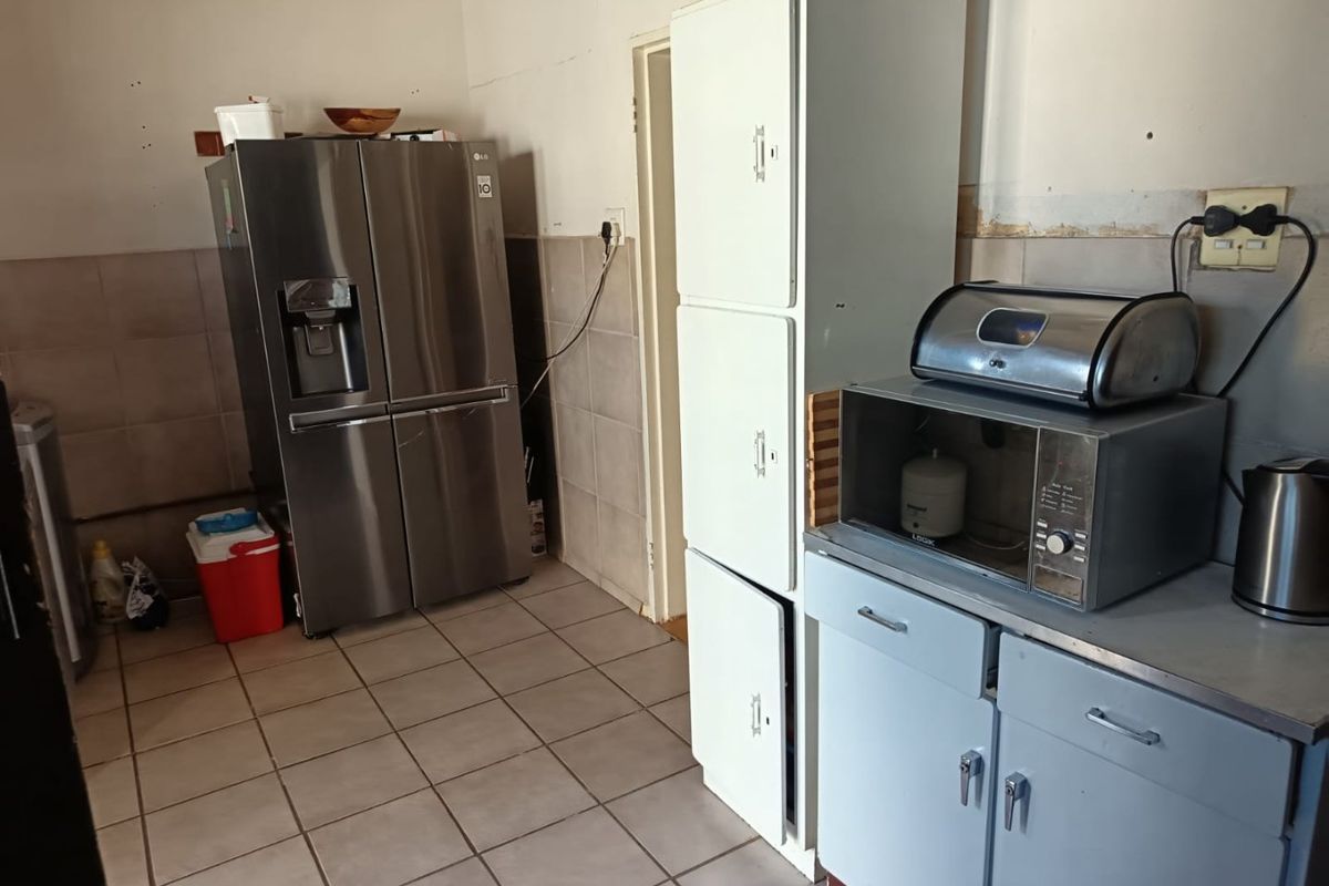 A functional kitchen area featuring tiled flooring, tiled splashbacks, and built-in cabinetry, currently showing signs of wear and requiring cosmetic updates.