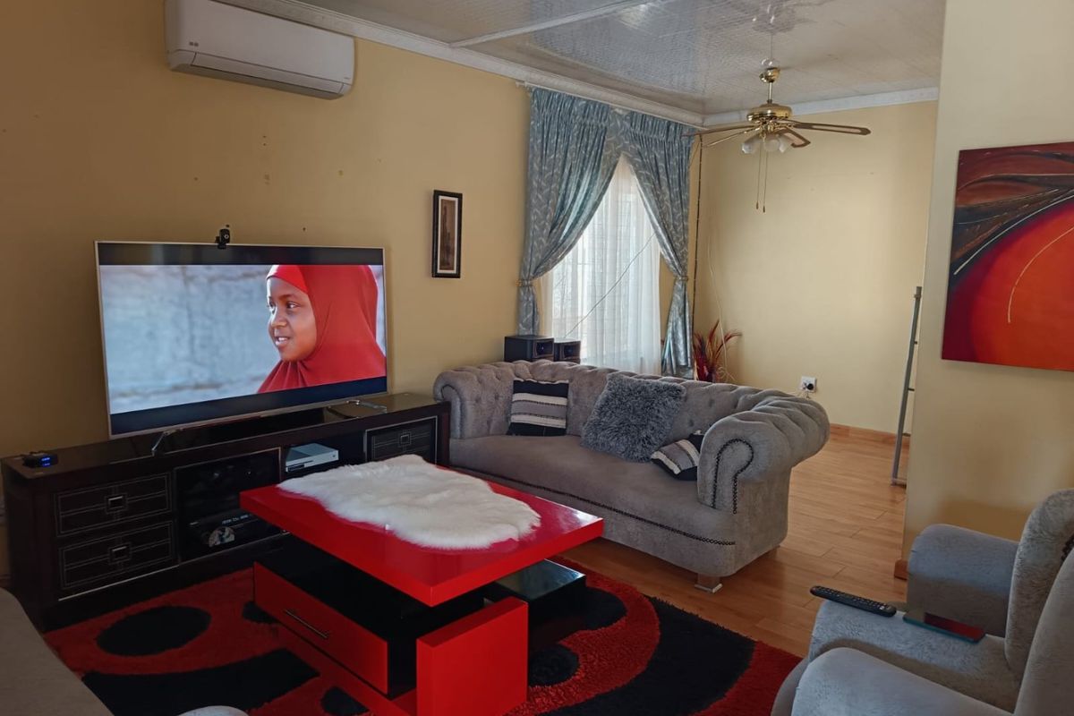 A comfortable living room featuring laminate flooring, a ceiling fan, and a wall-mounted air conditioning unit.