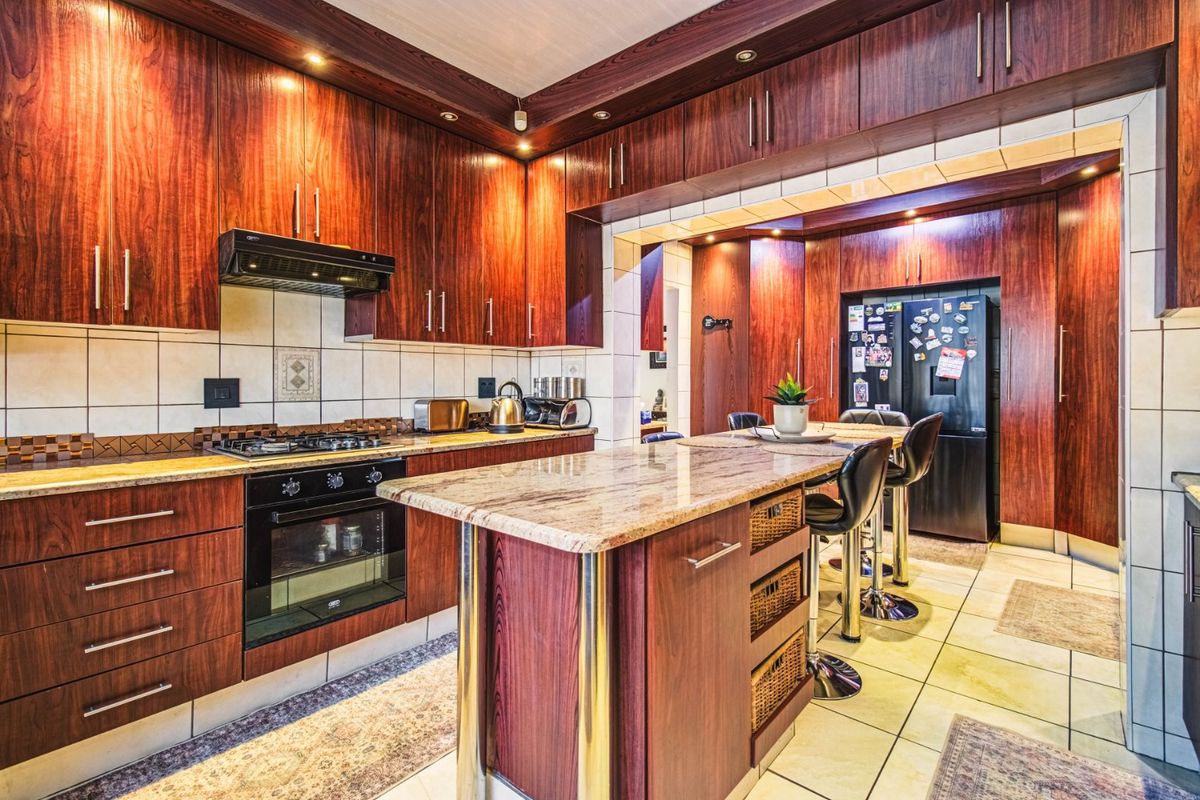 A well-appointed kitchen featuring rich wood-toned cabinetry, granite countertops, a central island, and integrated appliances, offering a warm and functional culinary space.