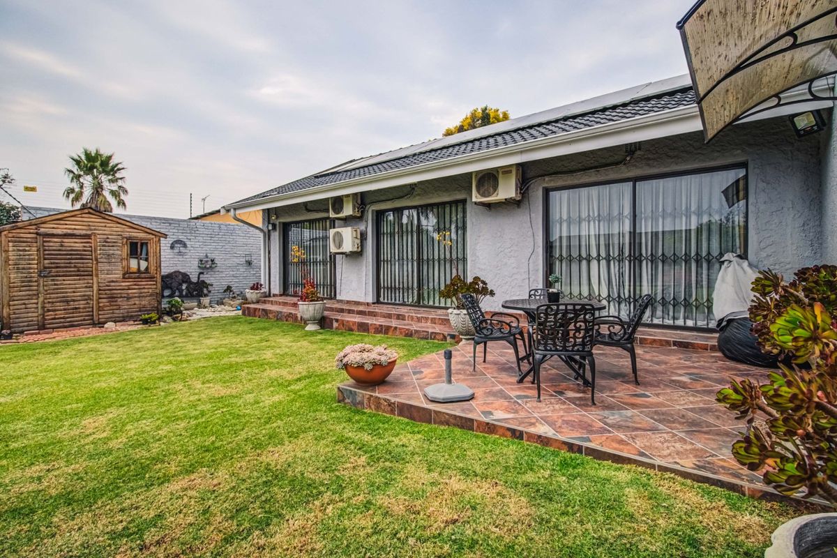 Rear exterior view featuring a tiled patio, sliding glass doors with security gates, air conditioning units, and a well-maintained garden with a wooden shed.