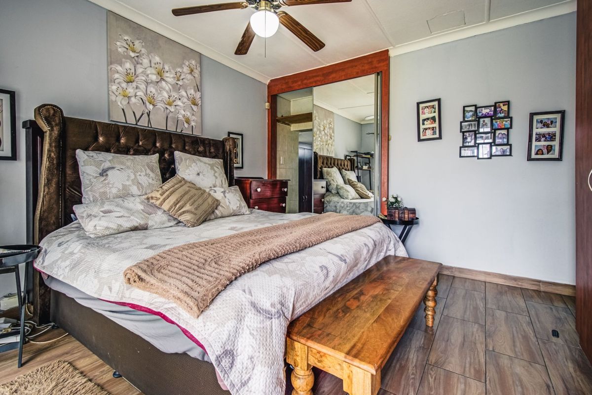 A well-maintained bedroom featuring tiled flooring, a ceiling fan, and large mirrored built-in cupboards providing ample storage space.
