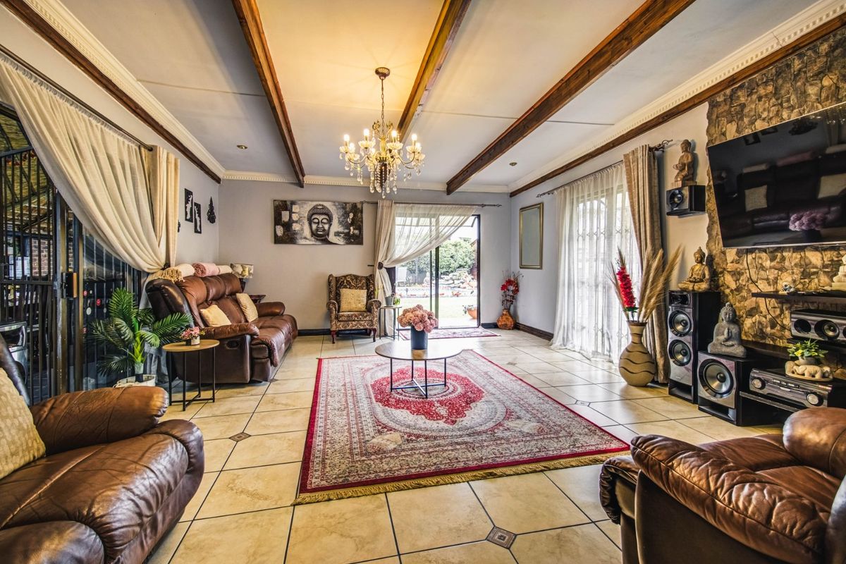 Spacious living room featuring exposed timber ceiling beams, a stone-clad feature wall, tiled flooring, and large sliding glass doors leading to the outdoor area.