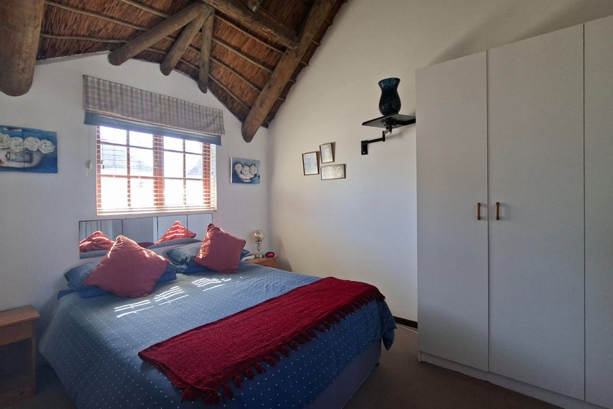 A cozy bedroom featuring a high vaulted ceiling with exposed timber rafters, thatched roofing, and a built-in wardrobe.