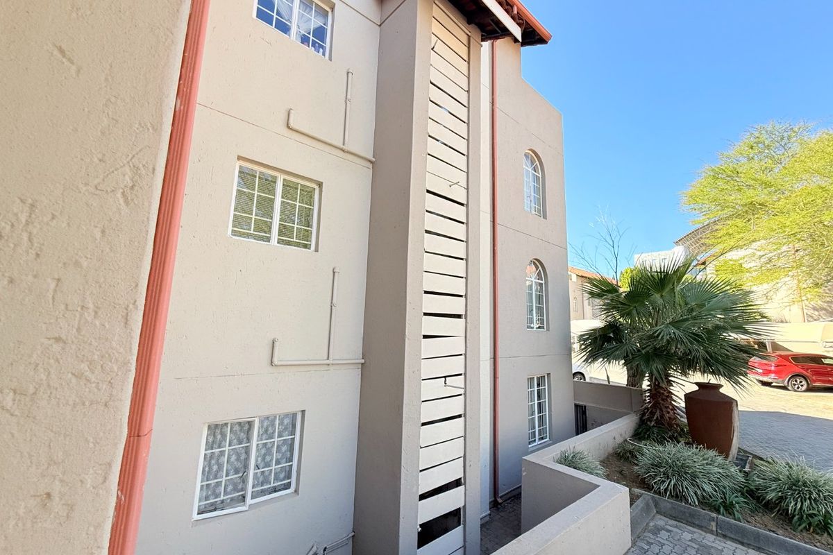 Exterior view of the apartment building facade featuring stucco finish, casement windows, and a vertical louvered screen element.