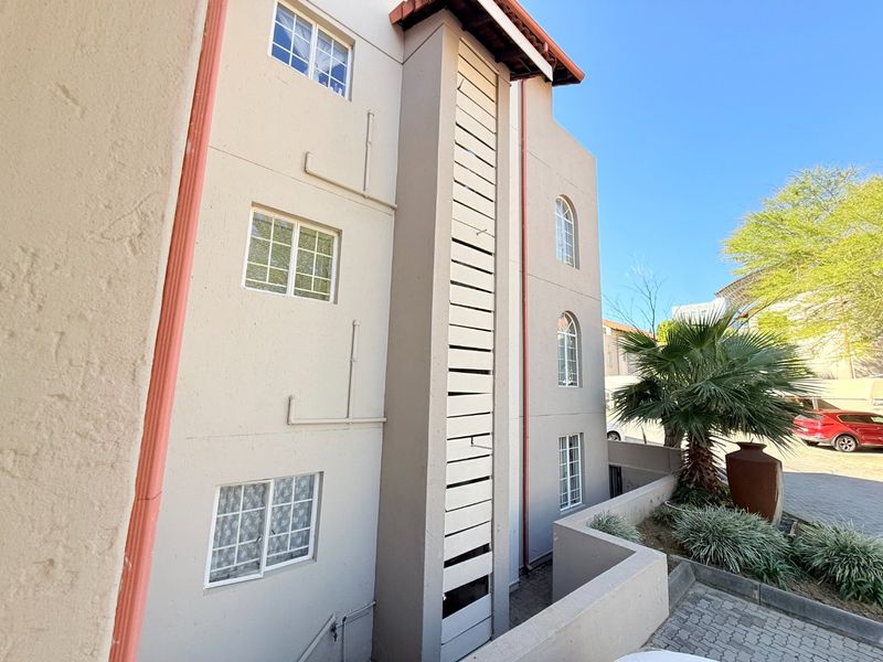 Exterior view of the apartment building facade featuring stucco finish, casement windows, and a vertical louvered screen element.