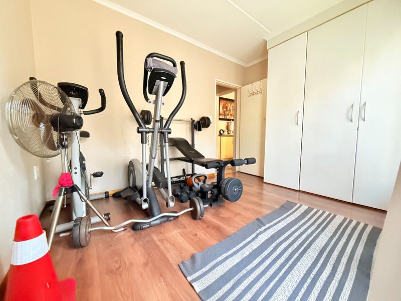 A bedroom featuring laminate flooring and built-in cupboards, currently utilized as a home gym space.